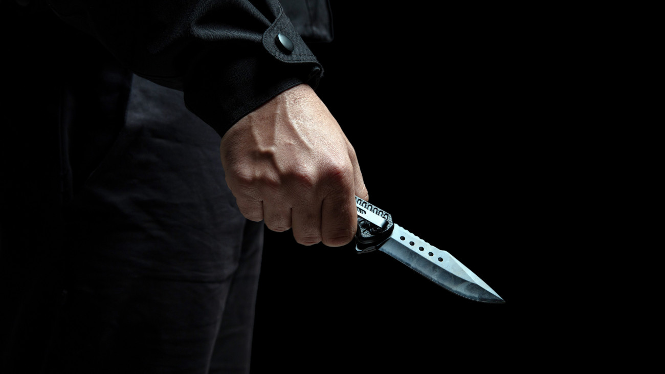 Criminal holding a knife closeup view, black background, armed attack concept.